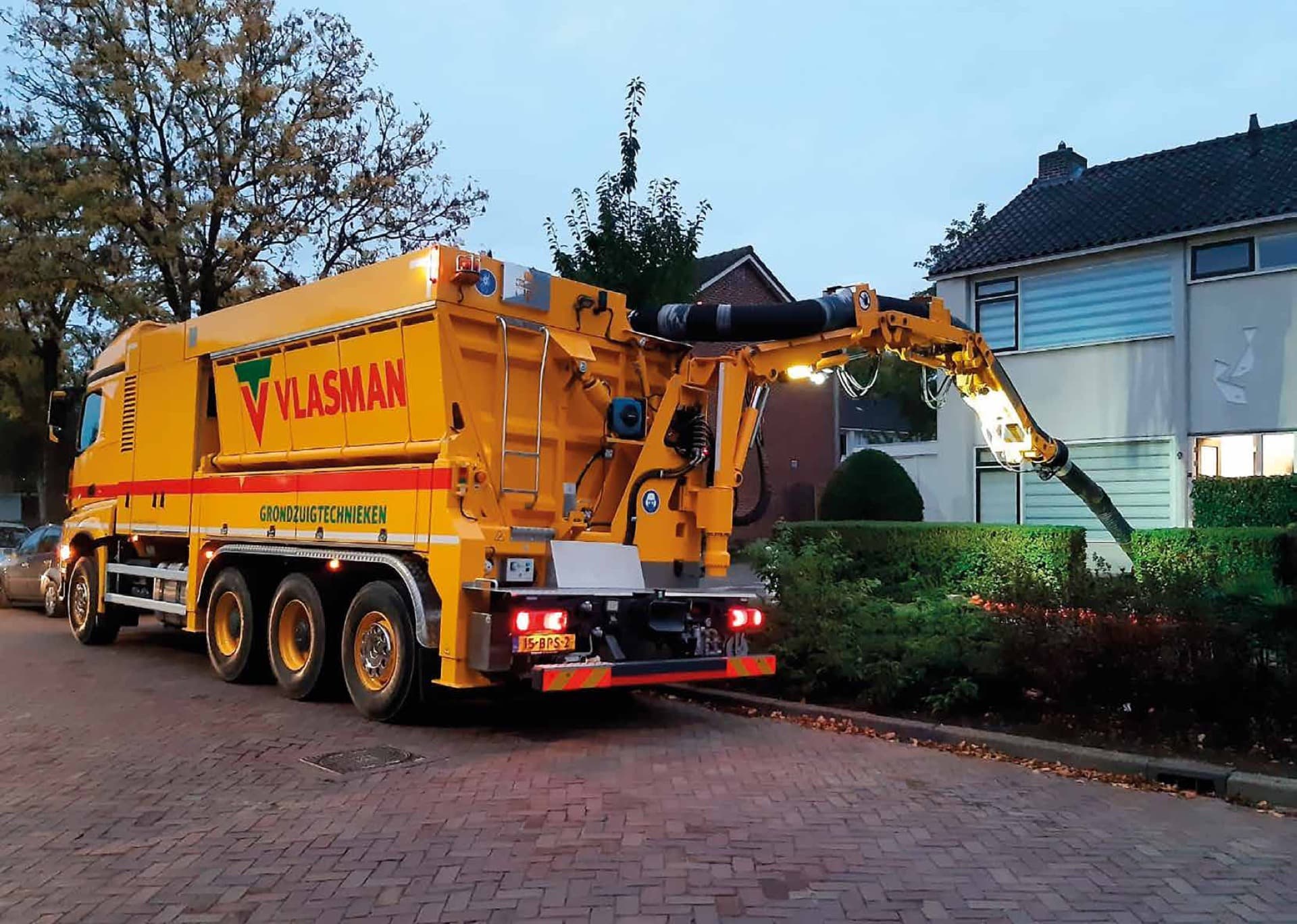 De gele Vlasman-grondzuigwagen aan het werk in een woonwijk
